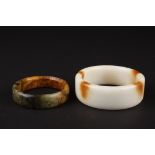 A large 20th Century Chinese white and brown polished stone bangle and another spinach and ochre