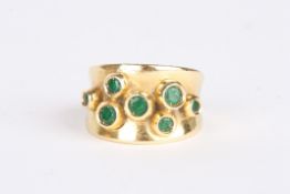 An 18ct gold and emerald dress ringset with seven chenier set circular emeralds in a shaped 18ct