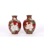 A pair of brass and enamel vases
of bulbous form, with blossoming flowers and butterflies on a red