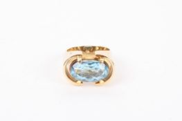 An oval blue topaz set ring of modernist design with yellow metal mount, mount scratched 9ct on