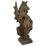 A large early 20th century carved wooden model of a heraldic griffin in seated pose and holding a