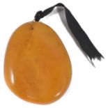 A large polished butterscotch amber pendant of natural form with yellow metal wire hanging loop.