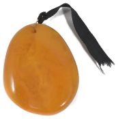 A large polished butterscotch amber pendant of natural form with yellow metal wire hanging loop.