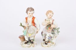 Two early 20th century German porcelain figures of a boy and girl seated holding flowers and