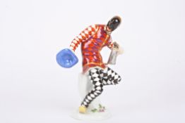 A 20th century Meissen porcelain figure of a harlequin holding jug and hat and seated on a