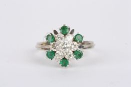 An emerald and diamond circular cluster ring with central seven stone raised diamond cluster