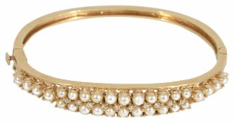 An Edwardian style pearl and diamond set gold hinged bangle having double row pearl set centre