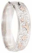 A hollow silver hinged bangle with gold overlay and scroll engraved decoration. Condition: Slight