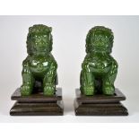 A pair of Chinese green glass lion figures with wooden stands imitating jade, H. 11cm.