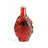 A Chinese carved red Peking glass snuff bottle of an Emperor in a landscape, H. 8cm.