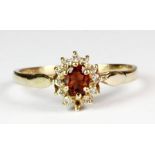 A 9ct yellow gold (stamped 375) garnet and diamond cluster ring, (M.5) (one small diamond missing).