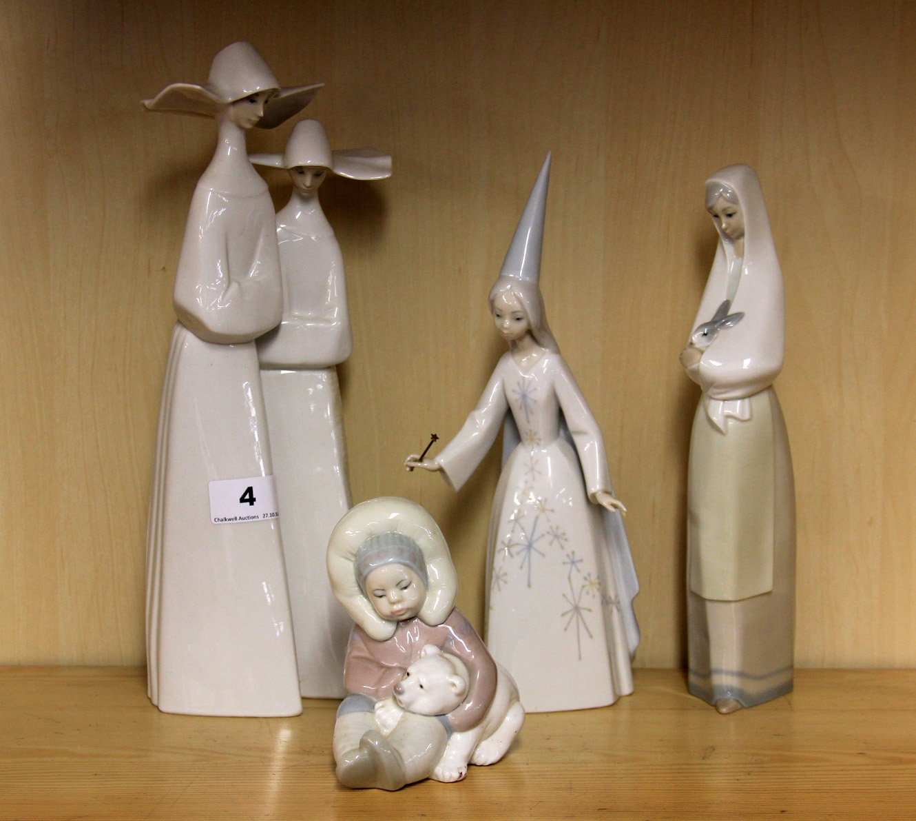 Three Lladro figures and a Nao figure of a girl with a rabbit.