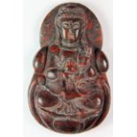 A Chinese carved red and black mottled hardstone amulet of a seated Guanyin.