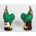 A small pair of Chinese brightly painted porcelain models of seated cockerals sitting on tree