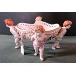 A German porcelain table centre, the oval central basket supported by four children,