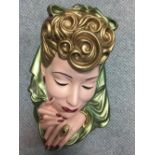 An Art Deco painted plaster figural mask, her golden hair partially covered by a green scarf,