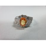 An orange sapphire and diamond ring, the oval cut light orange sapphire claw set between twin