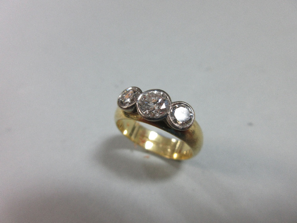 A collet set three stone diamond ring in 18ct gold, the graduated round brilliant cut diamonds