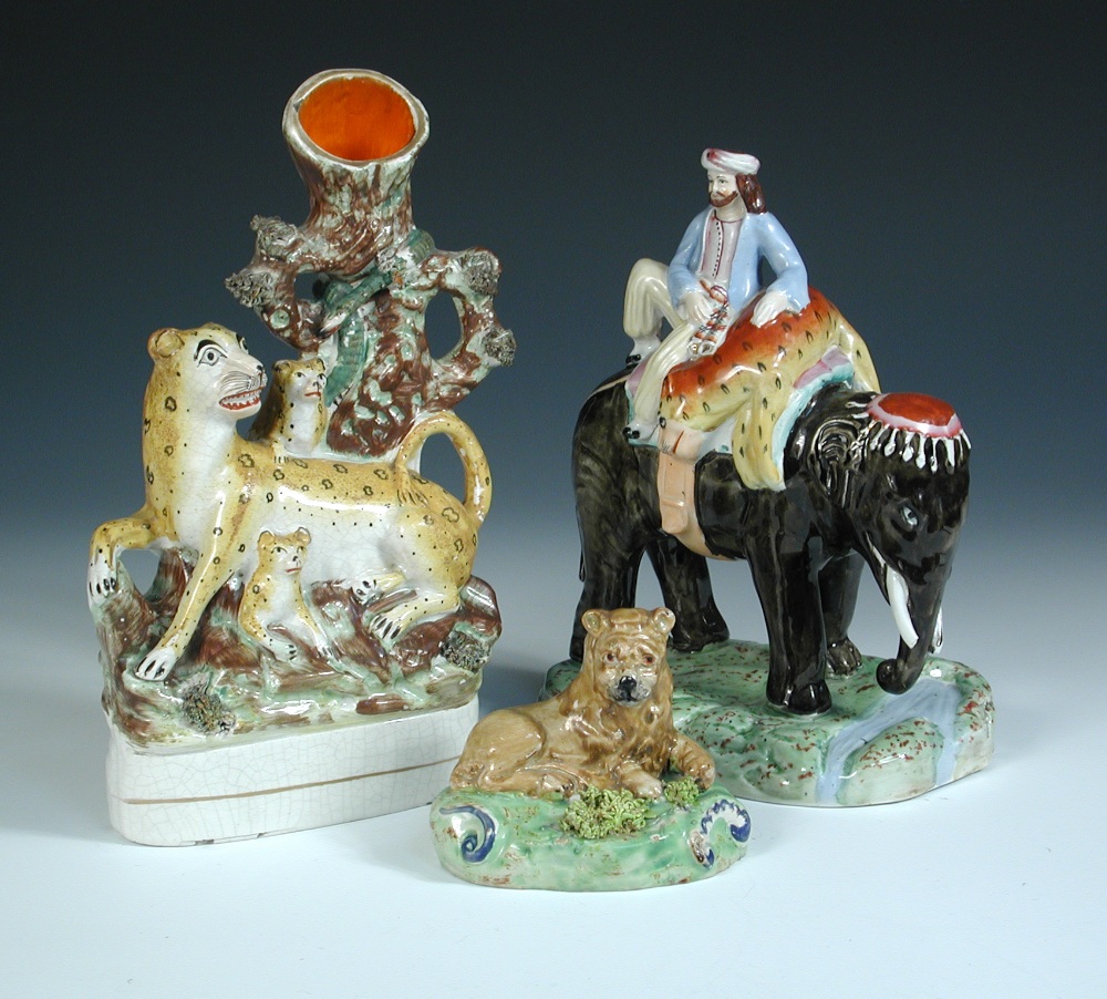 Three 19th century Staffordshire pottery figures, the 'Walton' lion reclining on a green mound,