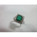 An emerald and diamond cluster ring, the square emerald cut emerald in a border of round brilliant