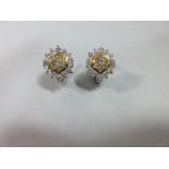 A pair of diamond and pale yellow diamond cluster earstuds, each with a round brilliant cut pale