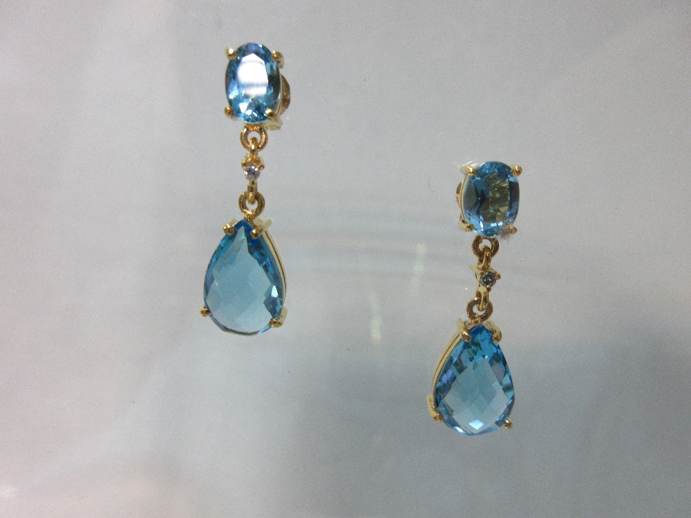 A pair of blue topaz earpendants with diamond highlights, each post headed by an oval cut blue topaz