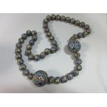 An Oriental enamelled bead necklace, the uniform 13mm beads, with two 27mm beads set near the front,