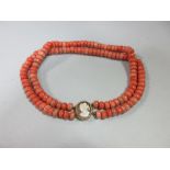 A hardstone bead necklace with cameo clasp, the double row of coral-coloured 10-11mm diameter tyre