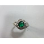 An emerald and diamond ring, the round cut emerald between two pear cut diamonds in overlapping