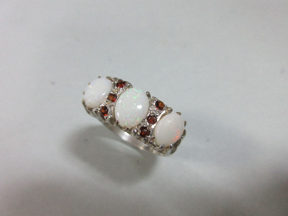 A three stone opal ring, the graduated oval cabochon opals spaced by lines of round cut garnets
