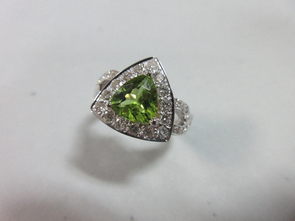 A contemporary peridot and diamond ring, the triangular cut peridot in a border of round brilliant