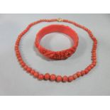 A graduated strand of coral beads and an early plastic carved 'coral' bangle, the necklace of