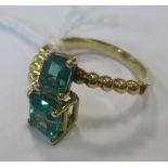 A two stone emerald ring, the two square step cut emeralds, each in a four claw setting, set to