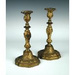 A pair of 19th century ormolu candlesticks, in the Rococo style with scrolling fronds on a scale