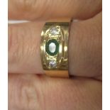 An emerald and diamond ring, the central oval emerald set to either side with a round brilliant