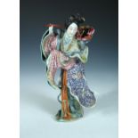 A 20th century figure of a lady, she stands wearing windswept colourful robes with a basket of fruit