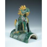 A pottery roof tile, probably Ming, the green glazed round arched tile surmounted by a seated