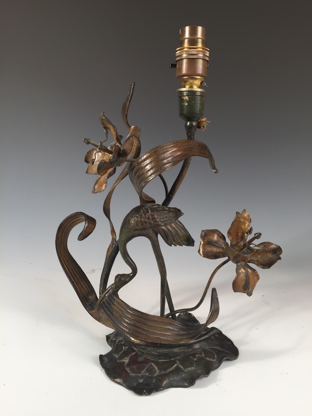 An Art Nouveau bronze lamp as a stork amidst foliage, modelled picking at leaves to a foliate