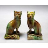 A pair of Whieldon ware cats, the seated felines facing each other on cushion bases, the dripping