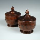 A pair of lignum vitae covered bowls, the covers with acorn finials, the hemispherical bodies with