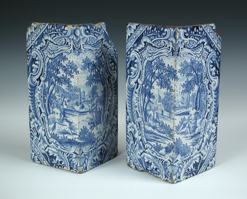 Two 18th century blue and white Delft corner stones from a stove, each with Rococo framed scenes