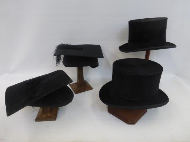 Two top hats and two graduation mortar boards on four wooden stands of varying heights.