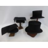 Two top hats and two graduation mortar boards on four wooden stands of varying heights.