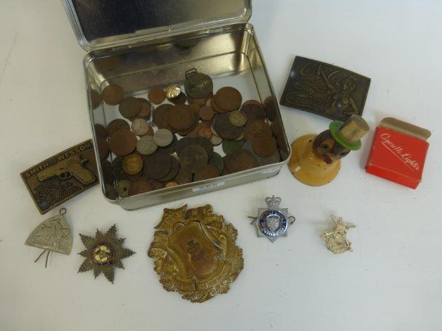 A tin of assorted coinage, military cap badges, belt buckles and an early 20th Century hand bell
