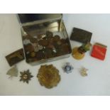 A tin of assorted coinage, military cap badges, belt buckles and an early 20th Century hand bell