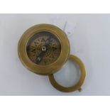 A brass tabletop compass with internal swivel magnifying glass.