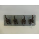 A set of four coat/cup hooks in the form of dogs' tails mounted on a slate wall plaque.