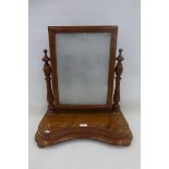 A Victorian mahogany toilet mirror raised on a shaped base to squat bun supports.