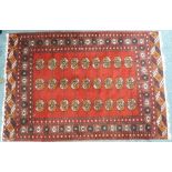 Tribal rugs; a red ground Bokhara rug with cream and ochre tekke set within a wide geometric border,