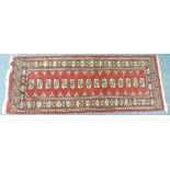 Tribal rugs; a red ground Bokhara runner with cream and blue tekke on a red ground set within a wide